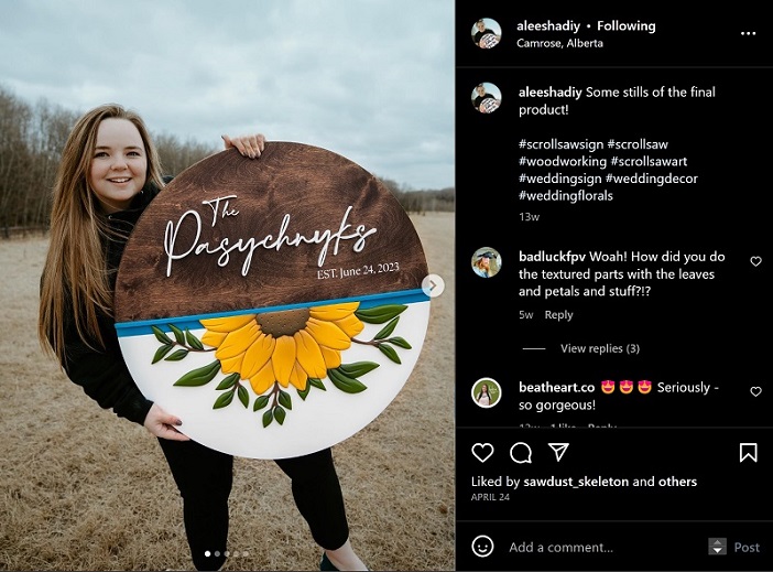 A light skinned girl with brownish blond hair holds a large sign. Half is wood grain and half has a large yellow sign flower. the edges of the sunflower are sanded to pop out. There is script font that says "The Pasychnyks"