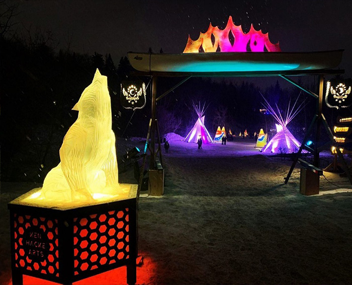 howling wolf light up sculpture made of layered acrylic. photo taken at night of an outdoor festival. In the background is a light up laser cut sculpture of a canoe. made on a Thunder Laser laser cutter machine.
