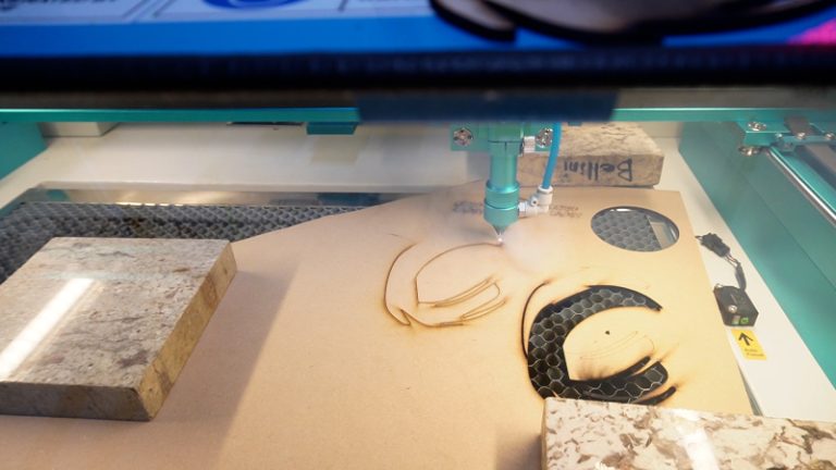 a close up image of the letter C being cut for custom wood signage on a laser cutter