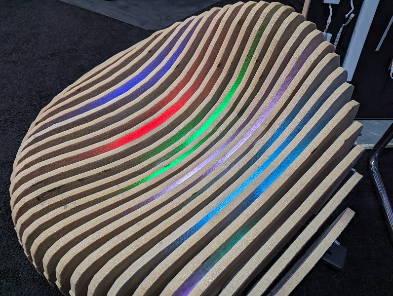 a rounded chair for festival furniture. A round design like a bean bean with an indent for sitting. the chair is made of wood using 3D slicing software and is composed of slices of wood anchored together with bolts There is light coming through each slice of the wood