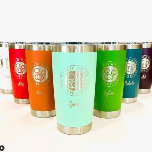 8 engraved metal coffee tumblers in rainbow colors: Right to left: white, red, orange, teal,green, blue, dark purple. Each mug reads Wind Rose Midwifery and has a logo. below each logo is a personalized name.
