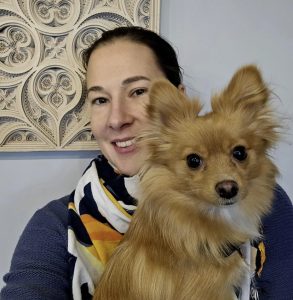 A light skinned woman with dark hair has a long haired pomeranian dog.