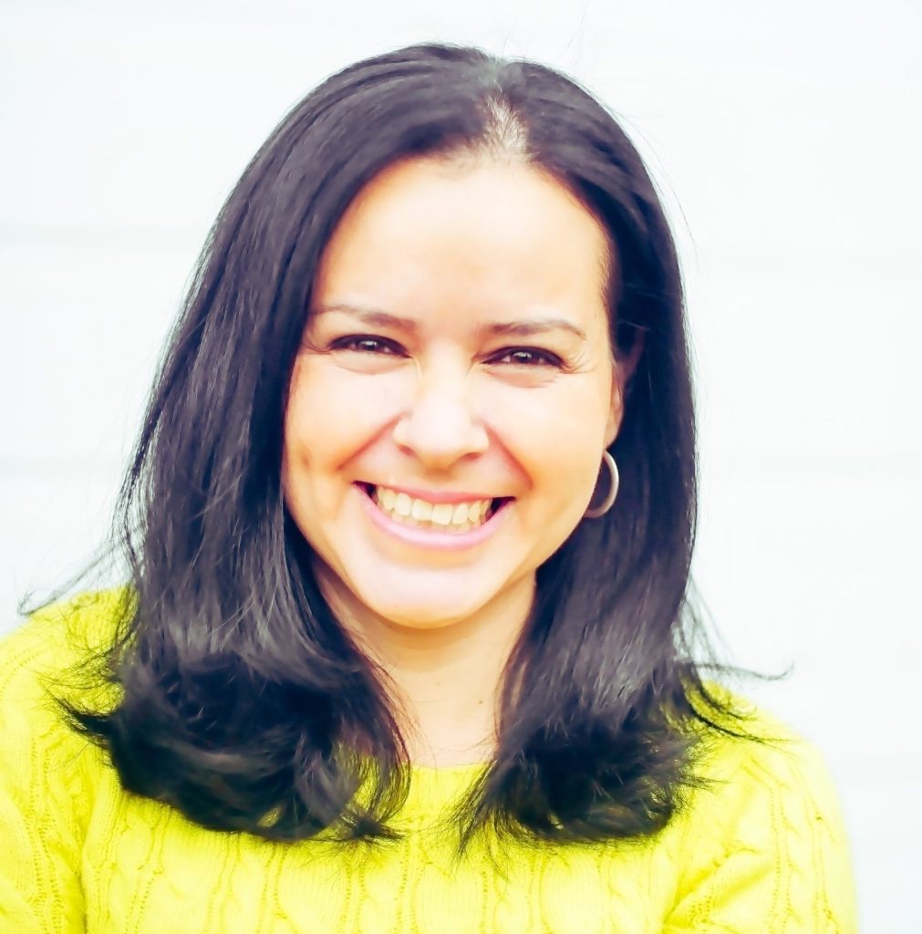 a woman with dark hair an light skin is smiling wearing a yellow shirt