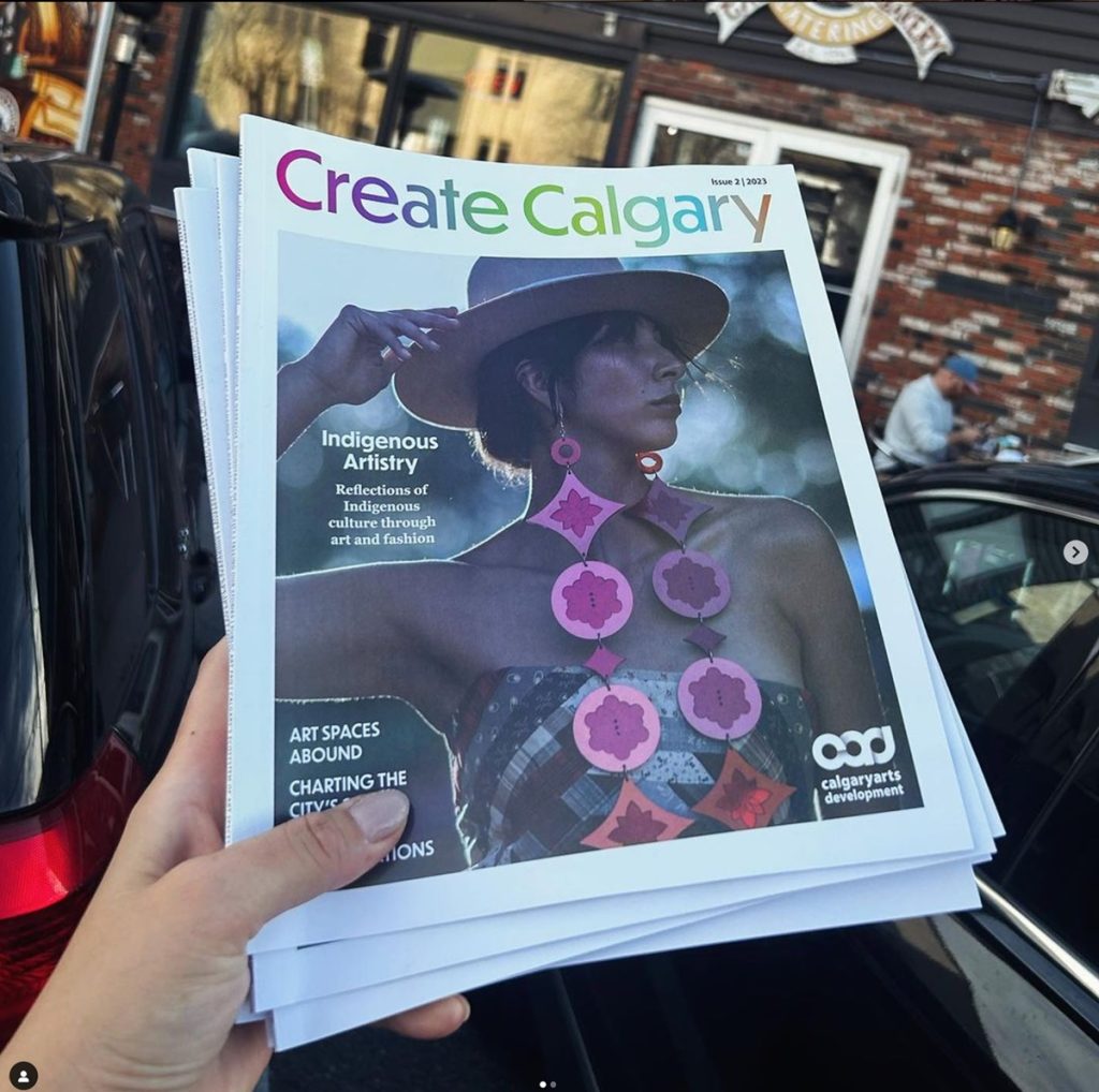 photo of a person holding a copy of create calgary magazine. Cover has an image of Indicity's model wearing long laser cut pinkish purple earrings