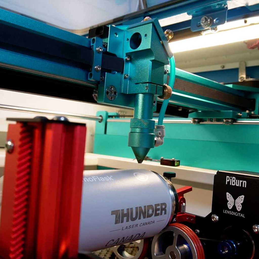 INSIDE A THUNDER LASER MACHINE: a red metal rotary device Piburn to engrave a white water bottle