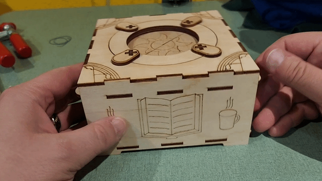 close up of a wood laser cut jewelry box with an iris opening on top being spun by a persons hands on a tabletop (gif)